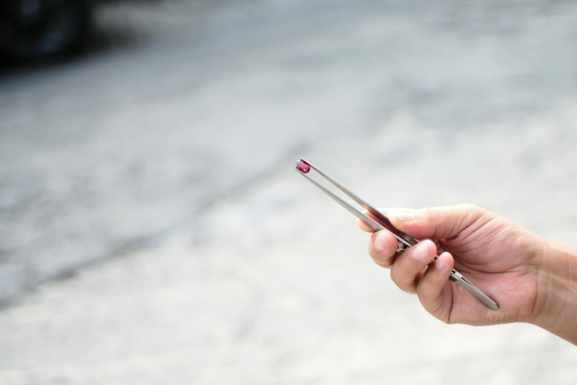 Dłoń trzymająca pęsetą kamień szlachetny w naturalnym świetle